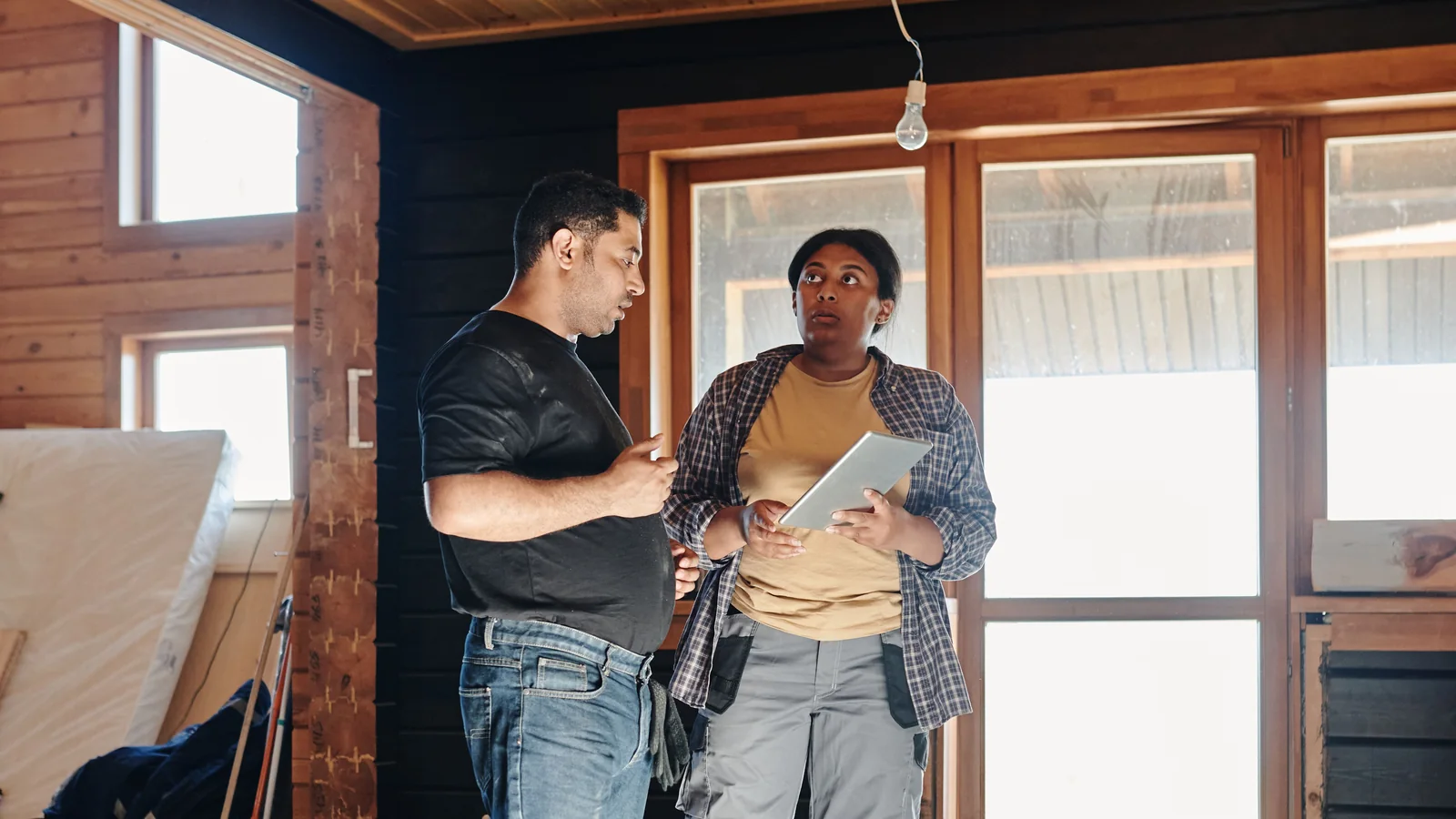Two adults discuss renovation inside a wood-lined room.