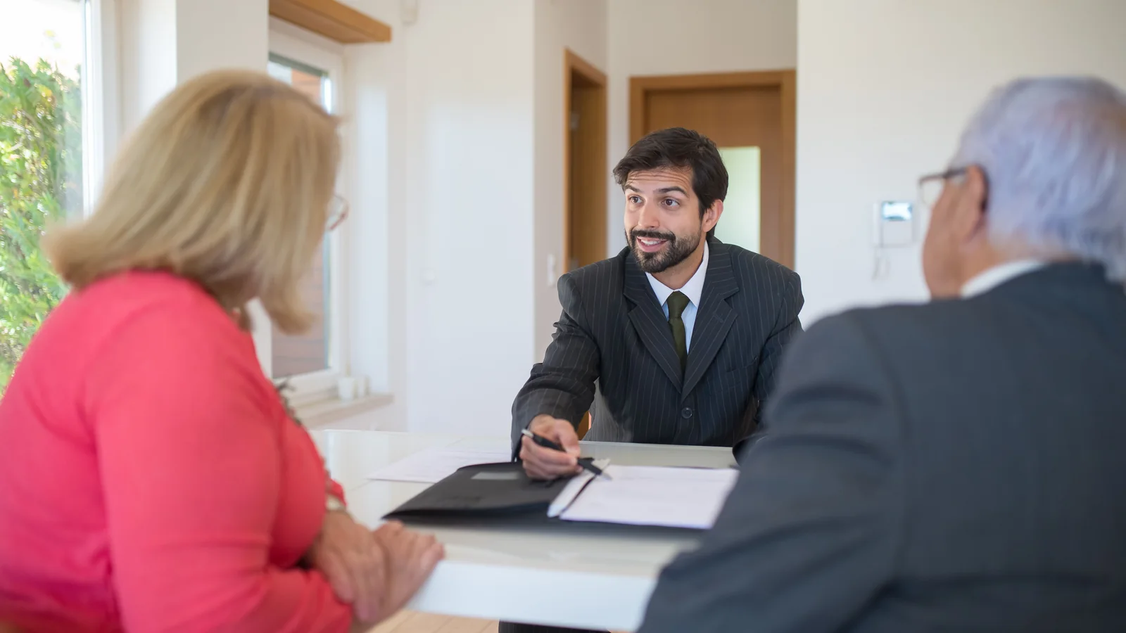 Three adults discuss paperwork across a desk.